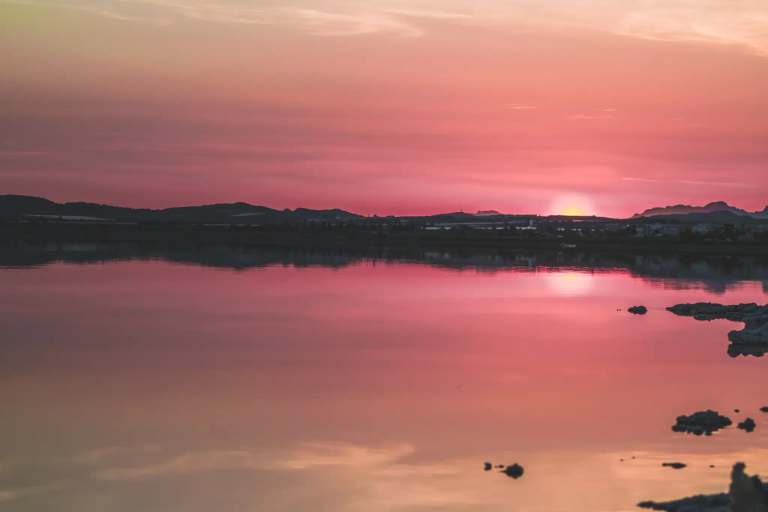 Torrevieja's roze zoutmeer bij zonsondergang, kalm water reflecteert de roze lucht met horizon