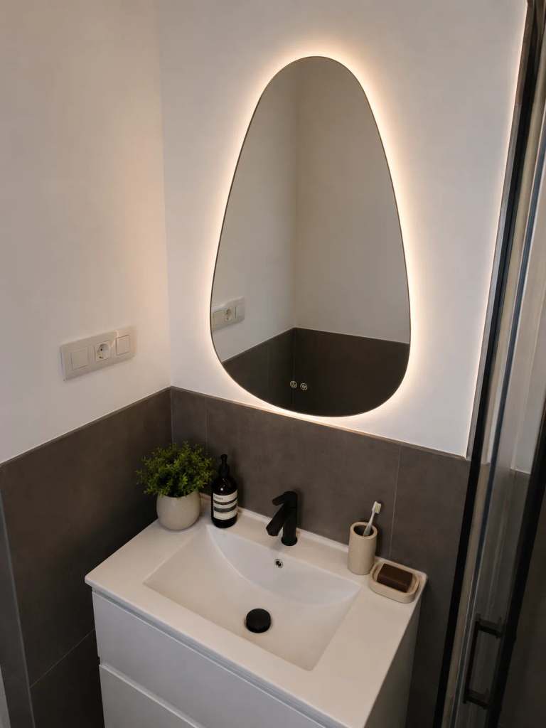 Moderne badkamer met strakke witte wastafel, zwarte kraan en een stijlvolle ovaalvormige spiegel met indirecte verlichting