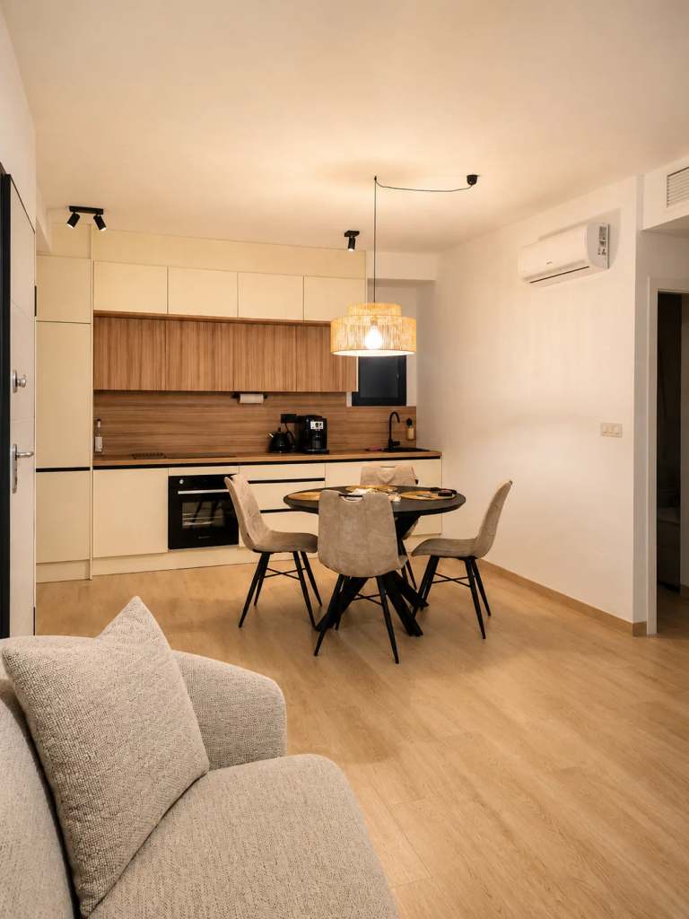 Moderne open keuken met eethoek, voorzien van licht hout en cremekleuren, en een comfortabele bank op de voorgrond