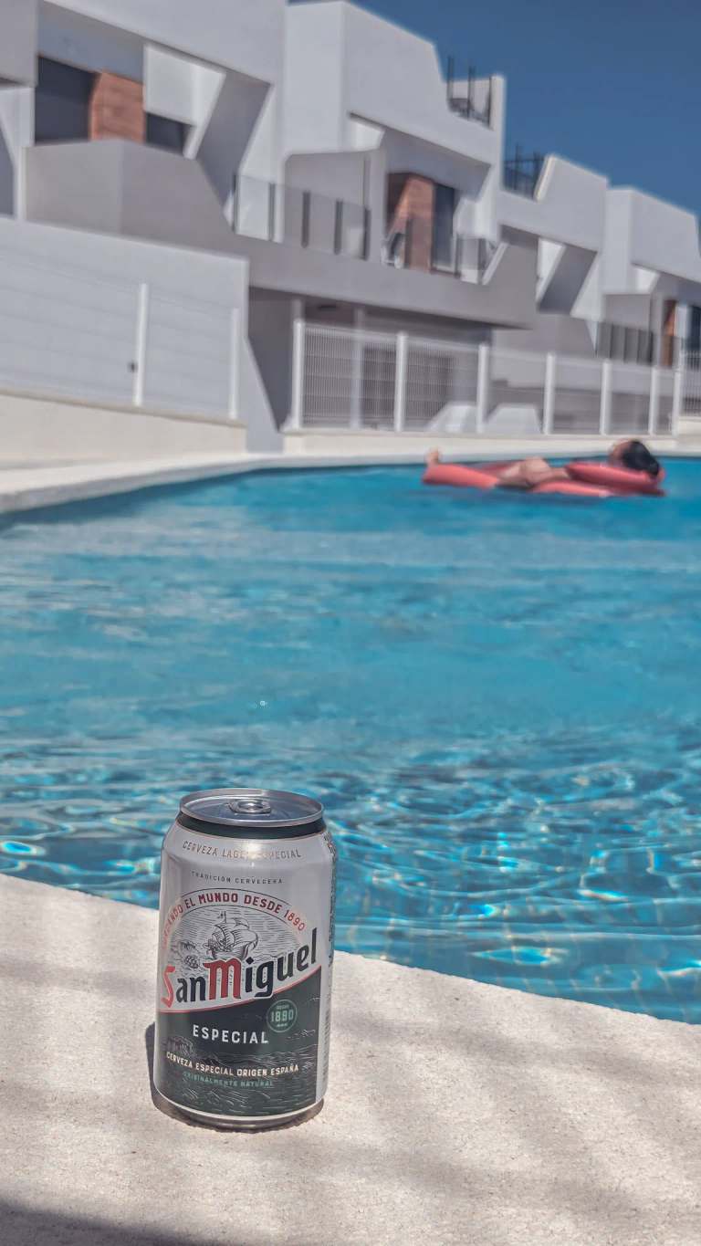 Koud Spaans bier aan de rand van het gedeelde zwembad, met iemand drijvend op een luchtbed in de zon
